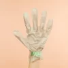 A hand holding a pair of Voesh Collagen Gloves with Cannabis Sativa Seed Oil on a beige background.