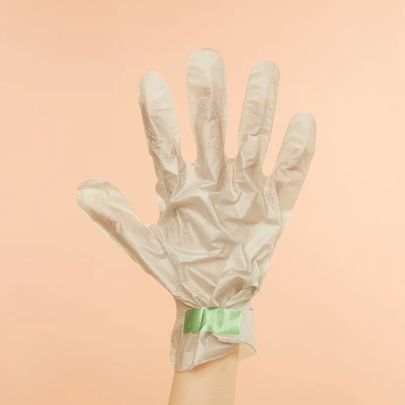 A hand holding a pair of Voesh Collagen Gloves with Cannabis Sativa Seed Oil on a beige background.