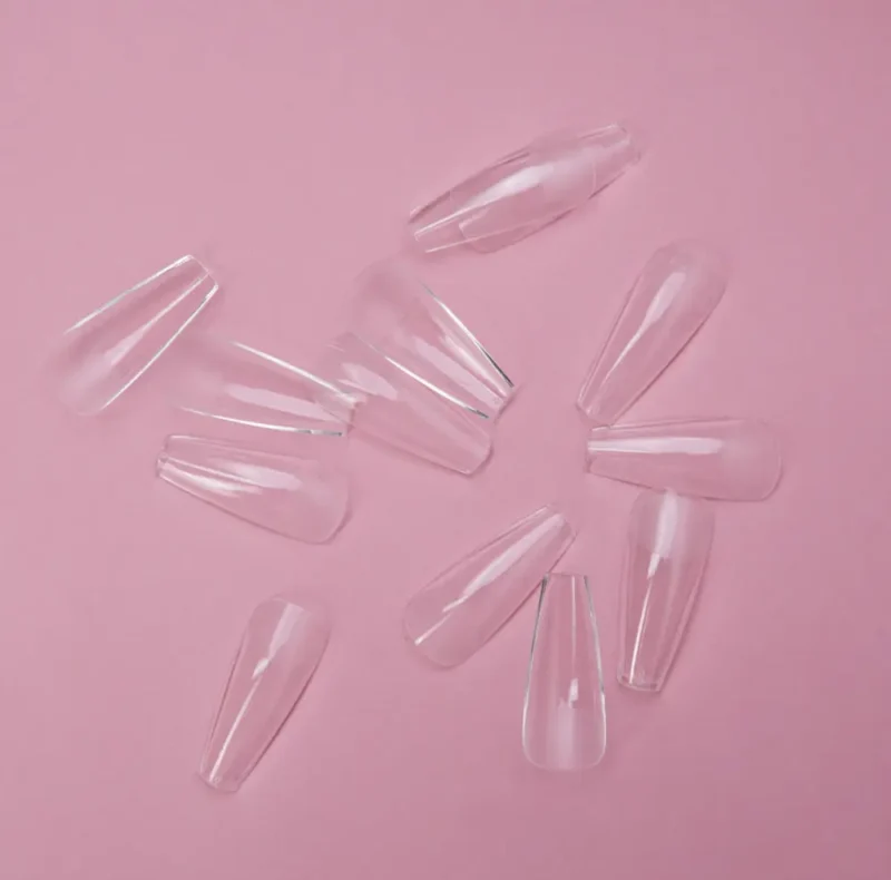 Transparent KYE Soft Gel Refill Tips - Long Coffin (50pcs/Bag) scattered on a pink background.