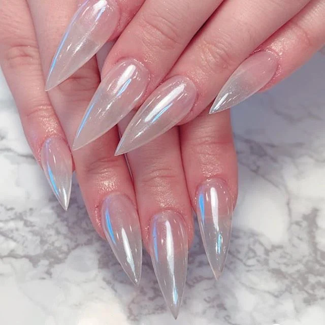 Close-up of hands with long, pointed, clear acrylic nails over a white and gray marble surface, enhanced with a stunning Cre8tion Nail Art Effect GLAZE 1g.