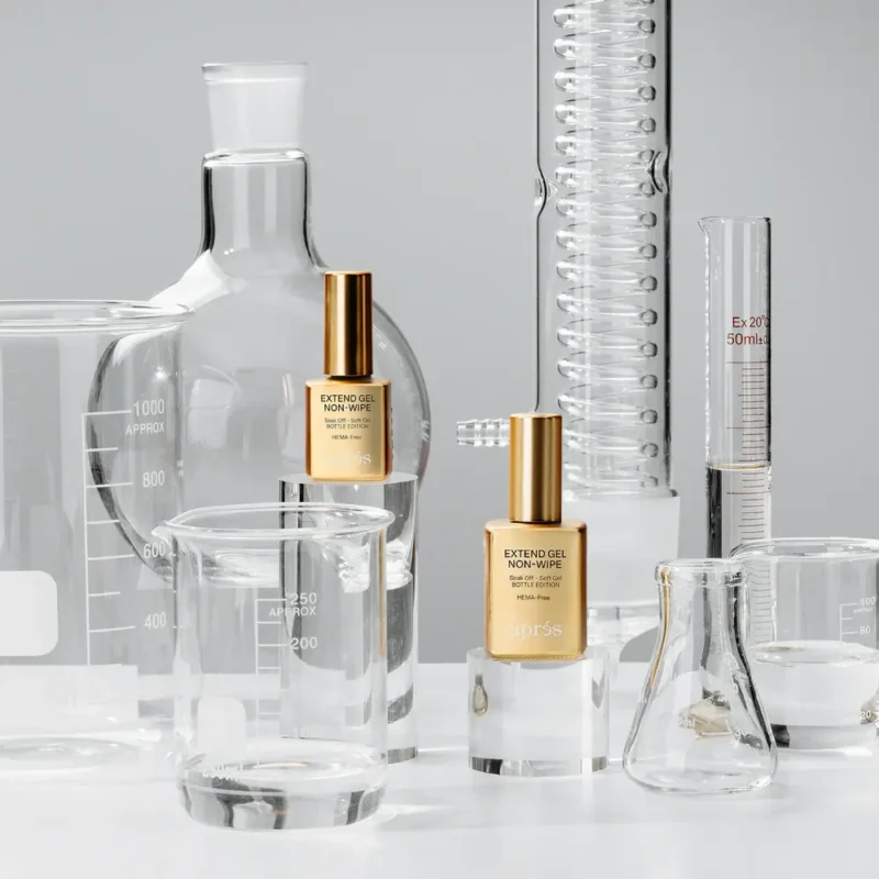 A scientific setup with lab glassware including beakers, flasks, and graduated cylinders, alongside two gold-capped bottles labeled "Apres Extend Gel Non-Wipe 15ml" positioned among the glassware.