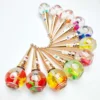 A set of twelve ballpoint pens arranged in a circle. Each pen has a clear, round top filled with colorful decorations and a gold-colored body, reminiscent of the elegant design seen in KYE Flower Cuticle Oil 0.9oz packaging.