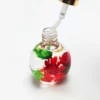 A round bottle of KYE Flower Cuticle Oil 0.9oz containing clear liquid with suspended red and green floral elements. The bottle is open, and a dropper with some liquid is inserted into it.