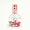 A round glass perfume bottle with a metallic cap, labeled "Apple," containing 0.9oz of liquid and colorful flower petals inside—perfectly embodying the essence of KYE Flower Cuticle Oil 0.9oz.