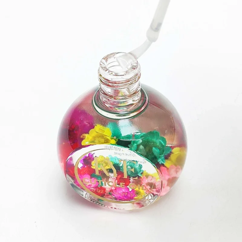 A round glass bottle filled with clear liquid and small colorful flowers, with a dropper inserted into the bottle, perfect for applying KYE Flower Cuticle Oil 0.9oz.