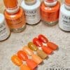 A display of orange and yellow nail polishes labeled "CHANCE Matching Trio - Autumn Spice Collection (36 Colors)" with matching artificial nail tips numbered 186 to 191, shown on a textured beige surface.