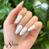 A hand with long, white, almond-shaped nails is displayed against a background of green foliage. The text "Cre8tion" appears, along with a small image of a jar labeled "Cre8tion White Silk Chrome Nail Art Effect 1g," showcasing the elegance of White Silk chrome nail art.