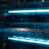 Close-up of two UV-C lights illuminating the interior of a DERMALOGIC UV Sterilizer 60L (SAAPP-60) chamber with reflective surfaces and wire racks.