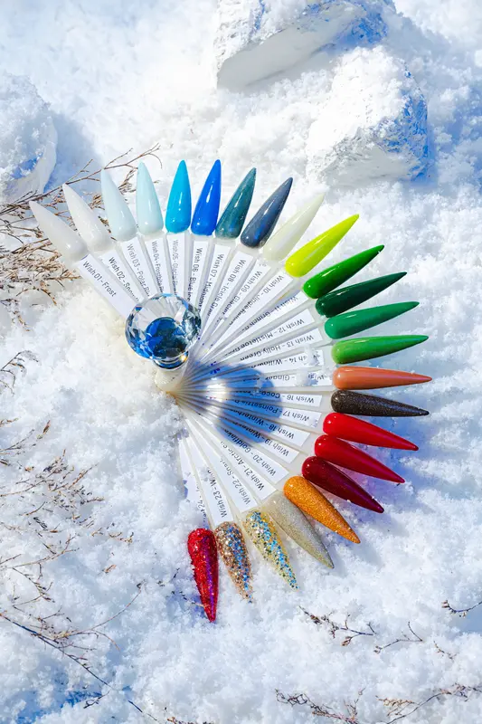 An impressive array of Nitro WISH Collection 3-in-1 Powder, Gel, & Lacquer in 24 colors is artfully arranged in a fan shape on snow, highlighting a range of vibrant hues and finishes.